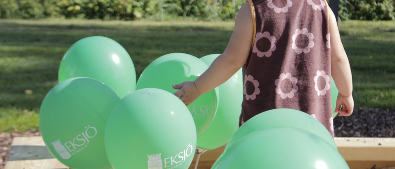 Ryggen på ett litet barn och flera gröna ballonger med Eksjö kommuns logotyp
