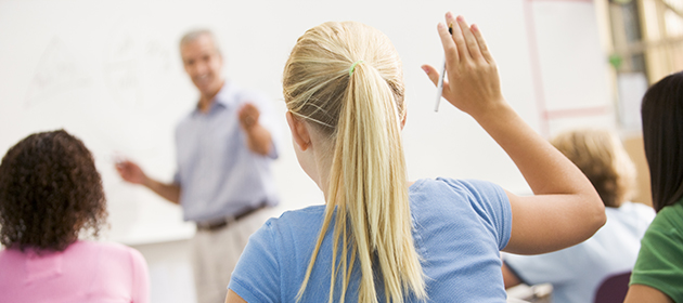Bild på ett barn i klassrummet som räcker upp sin hand