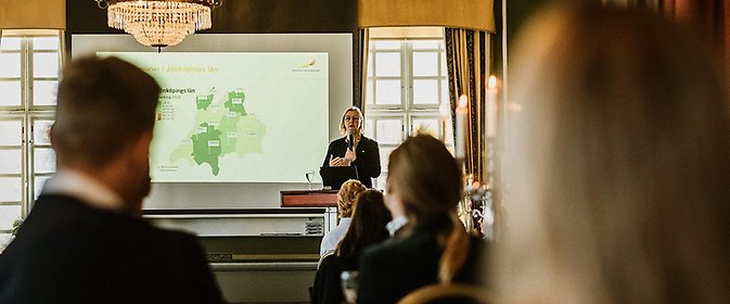 En kvinna som håller en presentation och en publik lyssnar.